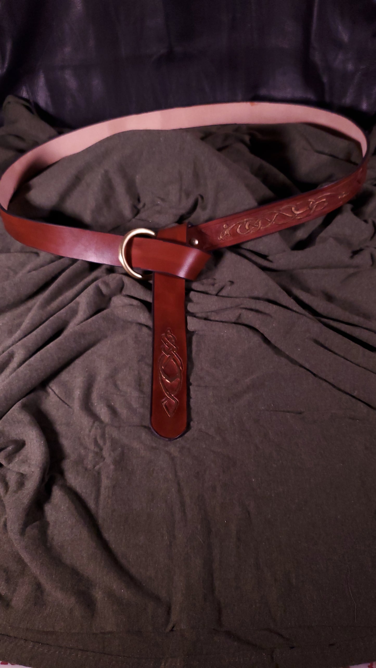 A tooled belt with an O-ring buckle. The belt is tied in a classic medieval style
