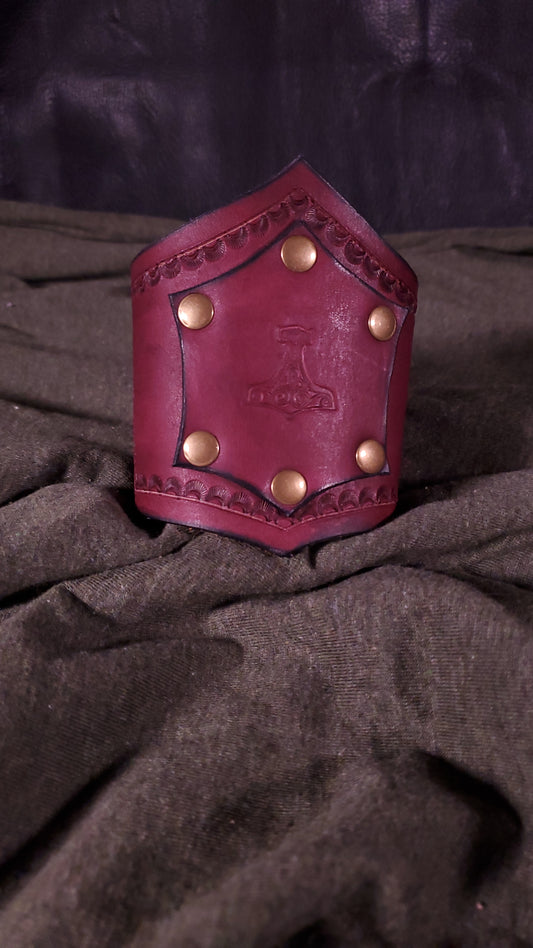 Red Cuff with a panel riveted onto it that has a mjolnir or thors hammer stamped onto it