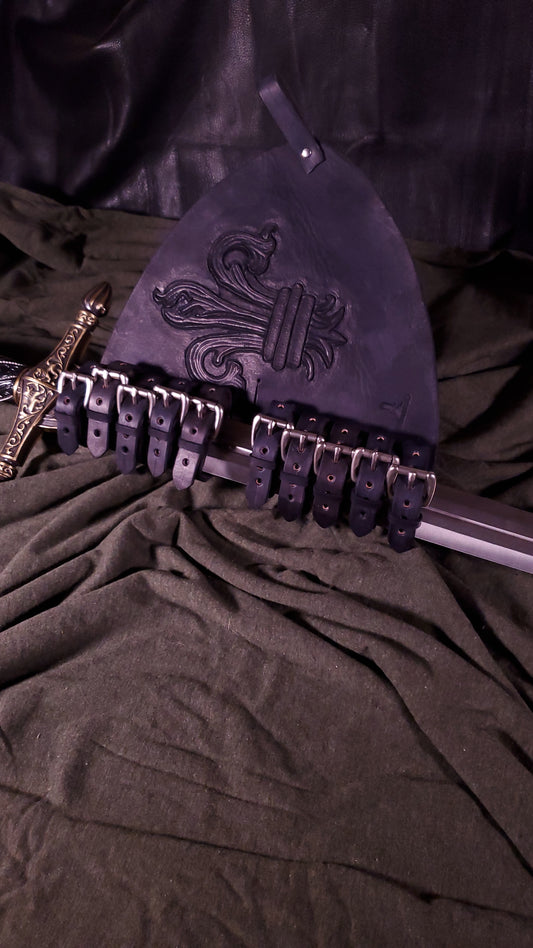A sword carrier with a longsword in it. the sword carrier has a large Fleur De Lis tooled on the face of it. It also has two belt loops at the top and side. It also has ten nickel buckles where the sword goes into to adjust for your specific sword.